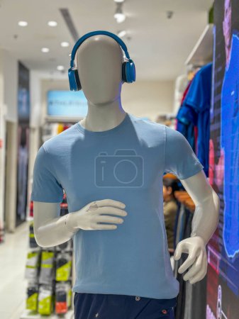 Un hombre con una camisa azul y auriculares azules se para frente a una pared de camisas