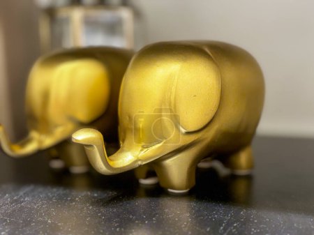 Two golden elephant figurines are sitting on a black table. The elephants are small and shiny, and they look like they are smiling. The scene is peaceful and serene