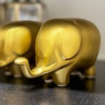 Two golden elephant figurines are sitting on a black table. The elephants are small and shiny, and they look like they are smiling. The scene is peaceful and serene