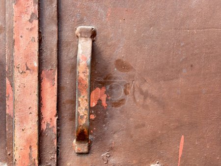 A rusty metal handle is on a brown surface. The handle is rusted and has a worn appearance