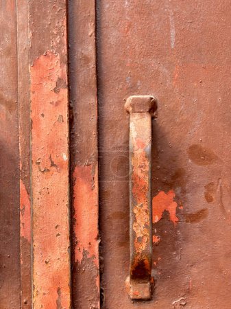 A rusty metal handle is on a brown surface. The handle is rusted and has a worn appearance