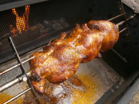 Téléchargez les photos : Outdoor party grilling chickens on charcoal. Three whole chickens on the grill on a spit, active burning coals in the grill. - en image libre de droit