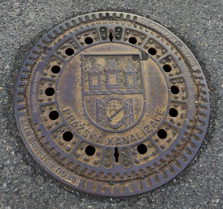Beautiful historical the lid of the canal in Prague on the street. Iron canal lid in Prague, Czech Republic with the coat of arms of the capital. Closed road sewer cover. Europe.
