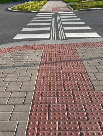 Der Weg auf der Straße. Markanter barrierefreier Übergang. Städtischer gepflasterter Bürgersteig und Fahrbahn mit Markierungen für behinderte Fußgänger.