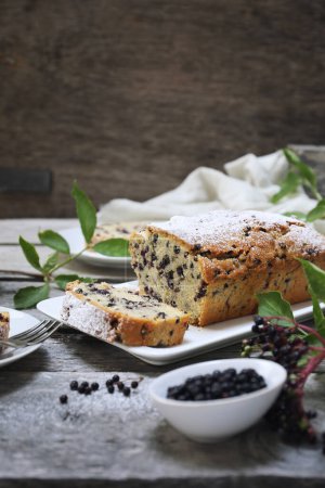 Summer baking. Black elderberry cake and and bunches of elderberries on grey wooden background 