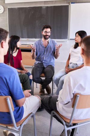 Photo for Vertical of Diverse group of high school students sitting on chairs in circle and interacting during a lesson, their Caucasian male teacher with them and talking Education concept. High quality photo - Royalty Free Image