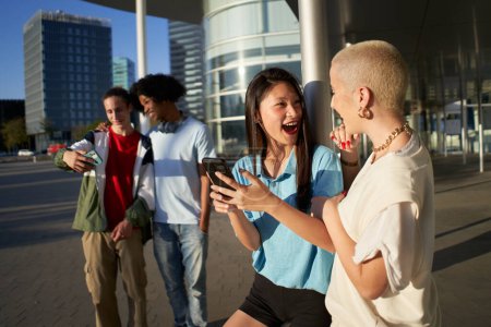 Photo for Multiracial people having fun together watching cell phone screens outdoors. Gen Z young students using smartphone and social networks together. High quality photo - Royalty Free Image