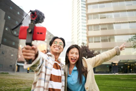 Photo for Asian people blogging outdoors. Selfie couple happy travel walk tourists taking photo with phone on city street panorama lifestyle. High quality photo - Royalty Free Image