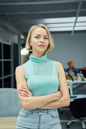 Photo for Vertical photo of serious confident blonde Caucasian business woman looking at camera standing with arms crossed in office. Executive CEO professional manager posing for business portrait. - Royalty Free Image