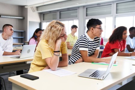 Gelangweilte Schüler, die mit einem Laptop im Klassenzimmer der High School sitzen. Studentengruppe einer Universität. . Hochwertiges Foto
