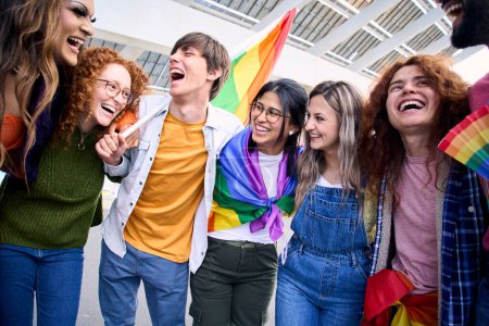 Group of excited young friends enjoying together on gay pride day. Joyful people gathered from LGBT community hugging laughing outdoors. Generation z and open minded. 