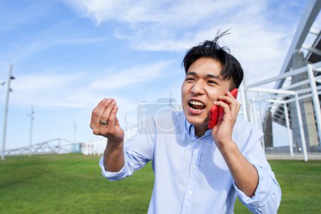 Photo pour Jeune homme asiatique en colère parlant sur son téléphone portable. Un Chinois agacé se dispute au téléphone. Homme excité communiquant. Les gens discutent en plein air attitude négative. - image libre de droit