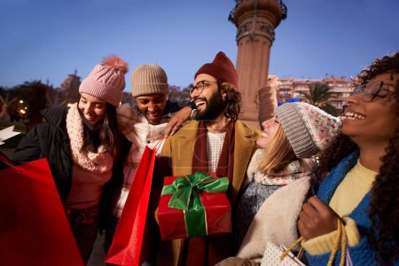 Photo for Smiling group diverse people holding black Friday winter christmas shopping bags gifts. Happy young millennial friends enjoying joyful outdoor together. Community, leisure and consumerism in sales. - Royalty Free Image