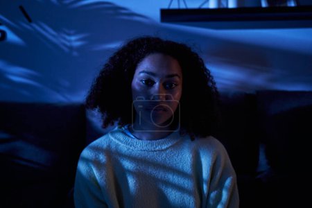 Photo for Portrait young black woman sad look sitting alone at home in dark night. Afro female depressive mental health problems and insomnia. Lonely, worried and pensive African girl in generation z people - Royalty Free Image
