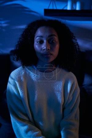 Photo for Vertical portrait young black woman sad look sitting alone at home in dark night. Afro female depressive mental health problems and insomnia. Lonely, worried and pensive African girl in gen z people - Royalty Free Image