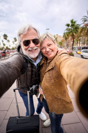 Photo for Vertical happy Caucasian senior tourist couple take selfie together. Man and woman smiling looking at camera enjoying pensioner journeys in European city street. Older people retirees sightseeing - Royalty Free Image