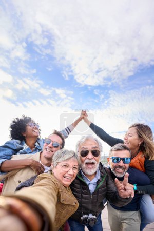 Vertikale Gruppe verschiedener lustiger, reifer Touristenfreunde, die huckepack mit in der Luft verbundenen Händen posieren und zusammen mit der Frontkamera Selfies auf Reisen im Freien machen. Erwachsene glücklich sechs aufgeregte Menschen genießen Ferien 