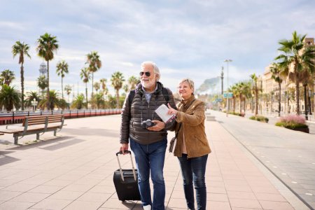 Photo for Older Caucasian tourist couple smiling looking and pointing interest places. Elderly woman and man standing in European city street enjoying pensioner vacation. Senior tourism people traveling happy - Royalty Free Image