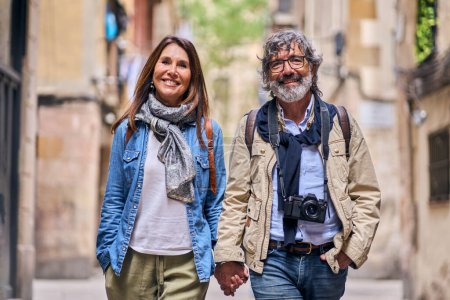 Porträt eines glücklichen älteren kaukasischen Paares, das Händchen haltend im Freien spaziert. Reife verliebte Touristen, die lächelnd in die Kamera blicken und ihren Urlaub genießen. Positive Beziehungen und Wochenendausflug