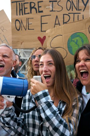 Mujer vertical gritando con megáfono en protesta contra la contaminación del planeta en la comunidad. Grupo de personas diversas quejándose enojadas en la demostración del calentamiento global con numerosas pancartas sobre el cambio climático