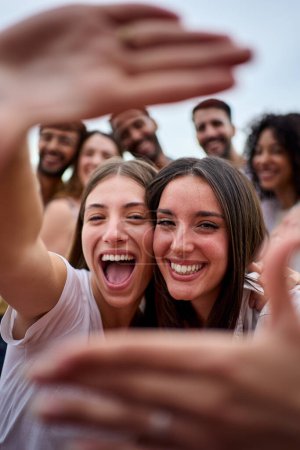 Photo for Vertical photo. Two girl friends making a frame with hands. A group of young people is happily celebrating, taking a selfie together. Smiling women having fun during their leisure travel - Royalty Free Image