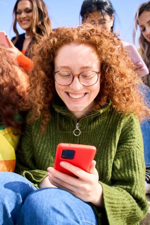 Verticale. Groupe de jeunes amis regardant téléphone mobile et célébrer la journée du festival de la fierté gay ensemble. Joyeuse communauté LGBTIQ vérifier les réseaux sociaux en plein air. Lesbiennes, gays et transgenres.