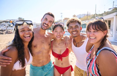 Fröhliches Porträt einer Gruppe verschiedener Freunde am Strand, die Spaß haben, während sie posieren und im Urlaub lächelnd in die Kamera schauen. Junge Leute in Badeanzügen in den Sommerferien