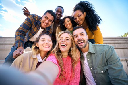 Photo for Group of multiethnic friends taking selfie with smart mobile phone outdoors. Happy young multiracial people smiling together looking at camera. University students having fun in college campus - Royalty Free Image