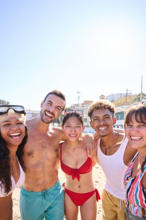 Fröhliches vertikales Porträt einer Gruppe verschiedener Freunde am Strand, die Spaß haben, während sie posieren und im Urlaub lächelnd in die Kamera schauen. Junge Leute in Badeanzügen in den Sommerferien