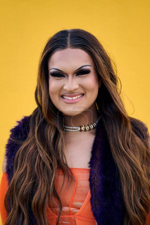 Vertikal. Porträt lächelnder Transgender mit gelbem Hintergrund. Glückliche Drag Queen Person posiert für Stolz Foto. LGBT und Trans-Community. Fröhliche Lateinamerikaner isoliert.