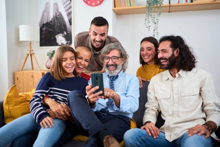 Kaukasische Mehrgenerationenfamilie versammelte sich im Wohnzimmer auf dem Sofa sitzend mit dem Handy. Glückliche Menschen lächeln mit einem lustigen Gesichtsausdruck und genießen und gucken lustige Videos zusammen in der Zelle zu Hause