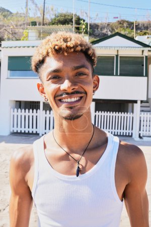 Vertical Portrait of happy young Latin man smiling looking at the camera on the beach. Holidays lifestyle of generation z people, vacations and summer in a beach coast town