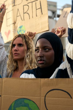 Vertical video. Serious Muslim woman holding a banner in a protest by a group of people at a demonstration on climate change and global warming, against pollution and factories