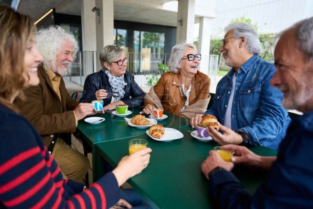 Mature gray hair friends group at coffee and bakery bar. Caucasian senior citizens people talking and having fun together at cappuccino restaurant. Life style of happy men and women at cafe terrace