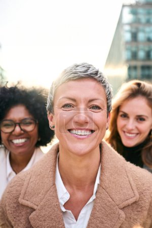 Foto de Vertical. Grupo de retratos empoderó a las mujeres de negocios de diversas edades que miraban sonriendo a la cámara con expresión feliz y segura. Caucásico atractiva mujer con pelo corto de pie en primer plano - Imagen libre de derechos