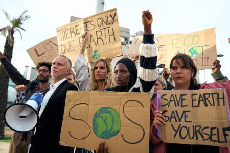 Serious Muslim woman holding a banner in a protest by a group of people at a demonstration on climate change and global warming, against pollution and factories
