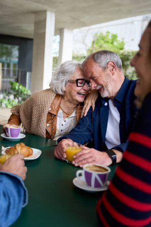 Vertical. Romance in the elderly. Group of happy residents friends of a geriatric. Mature gray hair at coffee bakery cafe terrace at nursing home having fun breakfast. Caucasian senior citizens people