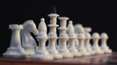 Close-up of white chess pieces along the board against a dark background. diagonal arrangement