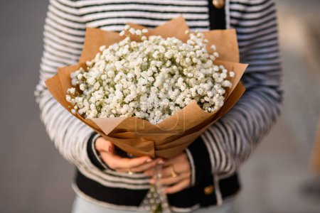 Selektiver Fokus auf einen Strauß schöner weißer Zigeunerblumen in Packpapier in weiblichen Händen. Nahaufnahme