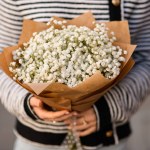 selective focus on bouquet of beautiful white gypsophila flowers in wrapping paper in female hands. Close-up