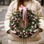 great round Christmas wreath of fir branches decorated with pink glitter balls and plants and bow in female hands