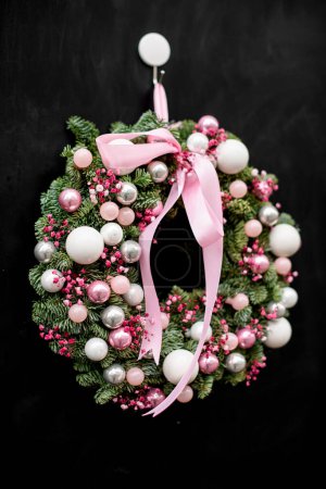 Close-up widok na piękne okrągłe Boże Narodzenie wieniec z gałązek jodły ozdobione różowe kulki brokat i różowe suche kwiaty i łuk na ciemnym tle