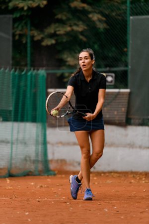 active female tennis player holding ball and racket and preparing to serve. Training at outdoor tennis court.