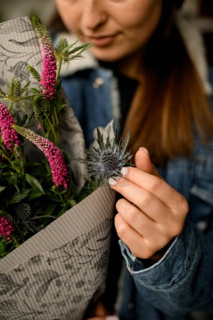 Téléchargez les photos : Photo recadrée de bouquet de fleurs avec chardon et lupin en papier d'emballage délicatement touché par la main féminine - en image libre de droit