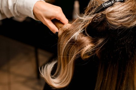 Téléchargez les photos : Close-up of hairdo making process. Hairdresser accurate puts long female hair with round comb. Hairstyle - en image libre de droit