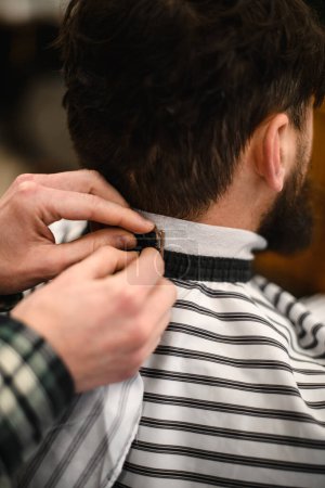 Photo for Cropped view of male barber hands gently fixing hairdressing collar around neck of man client. Barbershop concept - Royalty Free Image
