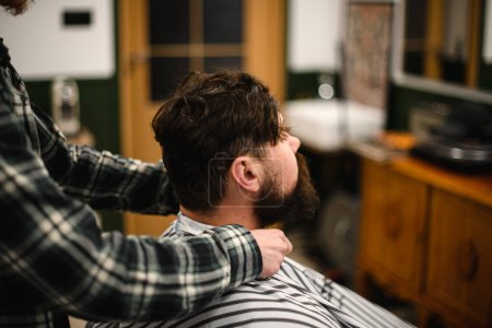 Photo for Side view on of male barber hands gently fixing hairdressing collar around neck of man client. Barbershop concept - Royalty Free Image