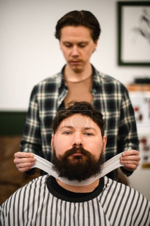 Photo for Front view on of male barber hands gently fixing hairdressing collar around neck of man client. Barbershop concept - Royalty Free Image