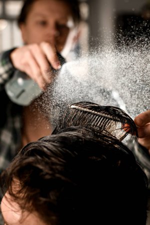 Téléchargez les photos : Gros plan des poils de tête d'un client masculin qui pisse par pulvérisation et peigne. Homme coiffeur faire coiffure masculine moderne - en image libre de droit