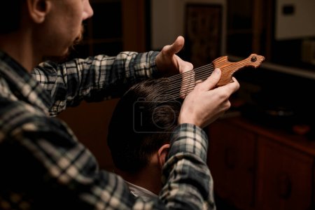 Photo for Male barber gently doing hair styling to a male client with an afropic comb with long metal teeth - Royalty Free Image